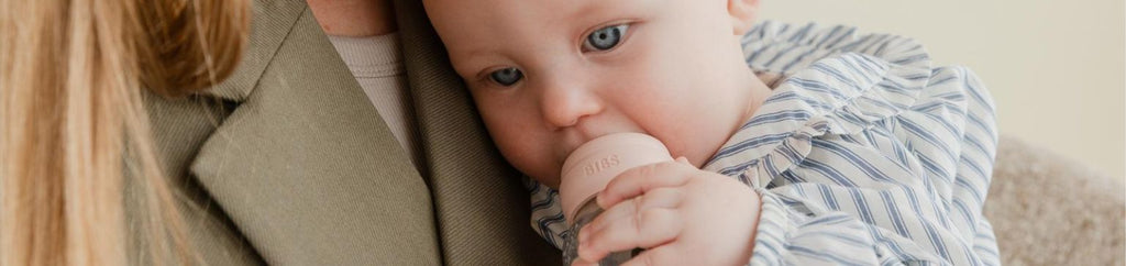 A baby being held and chewing on a bottle cap, illustrating a moment of comfort and bonding.