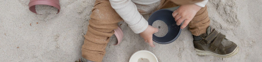 A toddler playing in the sand with bowls and cups.